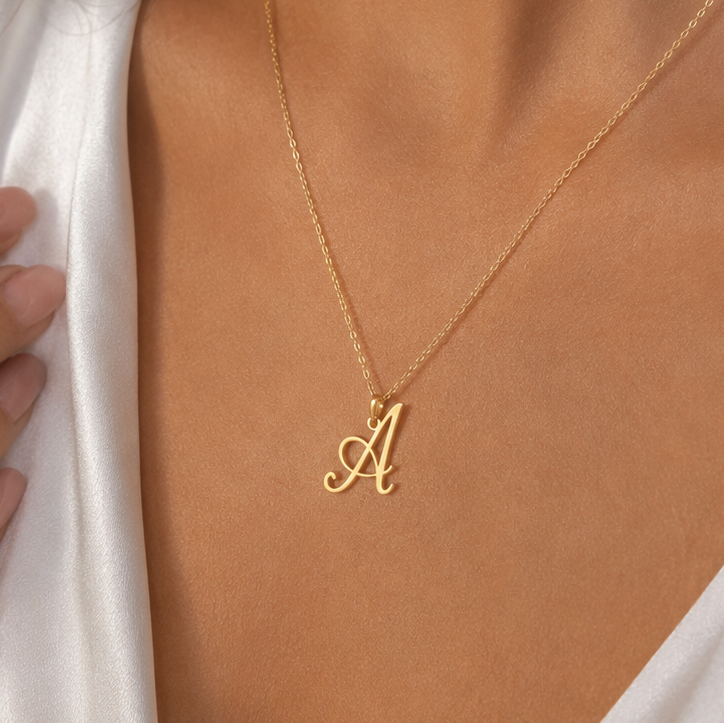 A delicate gold chain necklace with a cursive letter 'A' initial pendant, shown worn on a model's neck.