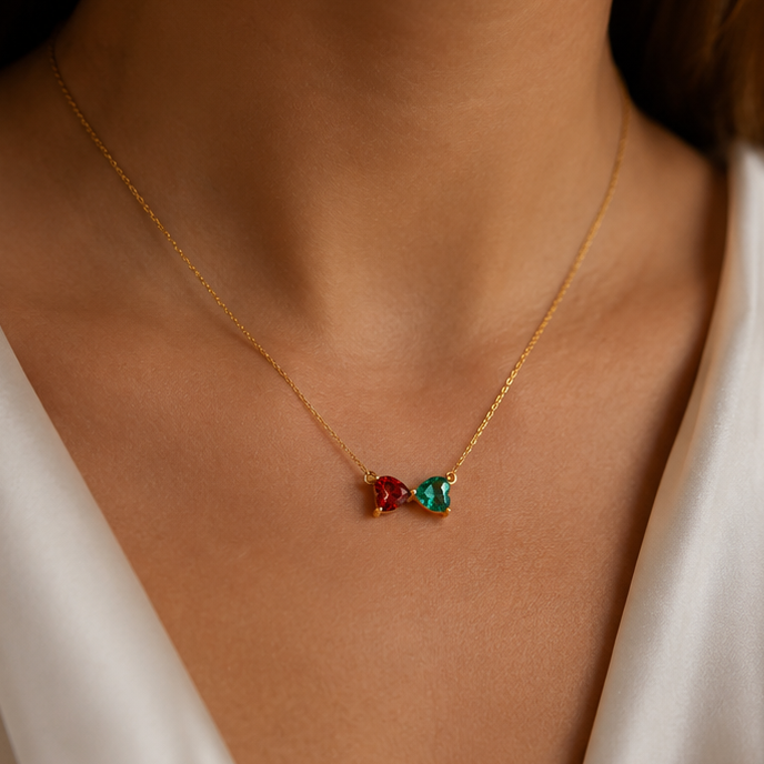A collage showing a gold necklace with two heart shaped birthstones featuring one ruby and one emerald, worn on a model's neck
