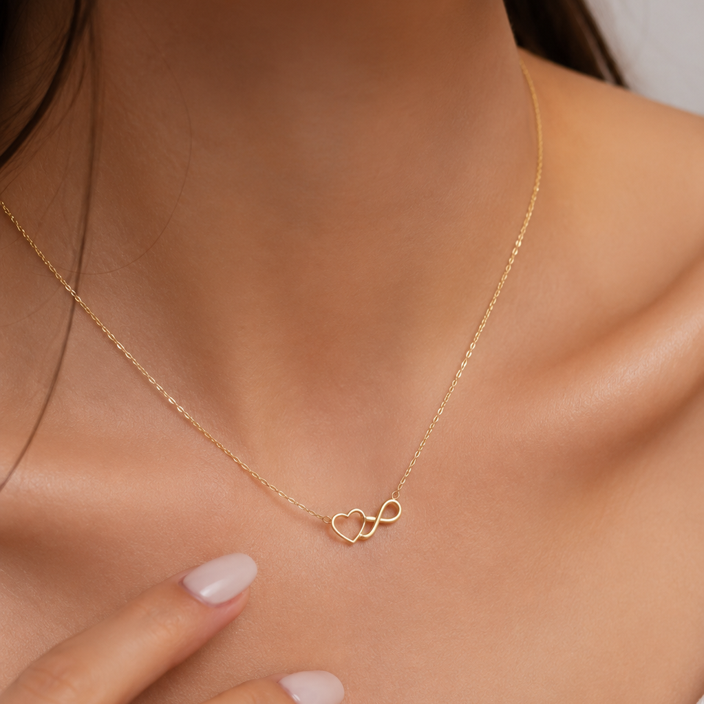A close-up of a model wearing a delicate gold chain necklace with a small infinity symbol pendant, styled with a hand resting near the chest.