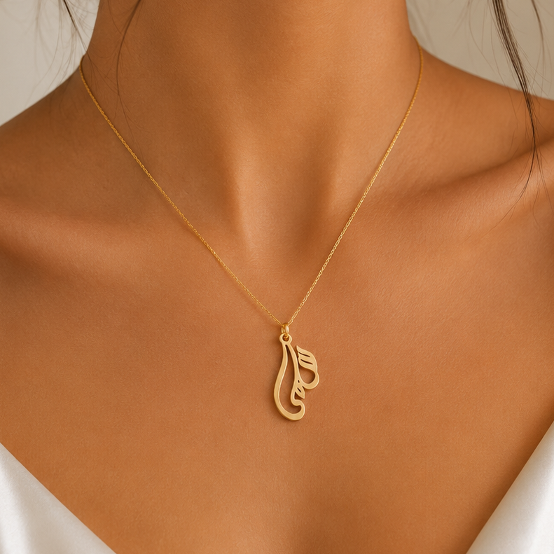 A close-up of a woman wearing a delicate Arabic name gold necklace with a calligraphy pendant, styled with a white satin camisole top.