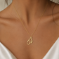 A delicate gold necklace with an Arabic calligraphy name necklace pendant is worn by a model in a white satin camisole top.