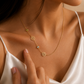 Woman wearing a personalised 18K gold Birth Flower & Birthstone Necklace with white satin dress and hand gently pointing to the necklace.