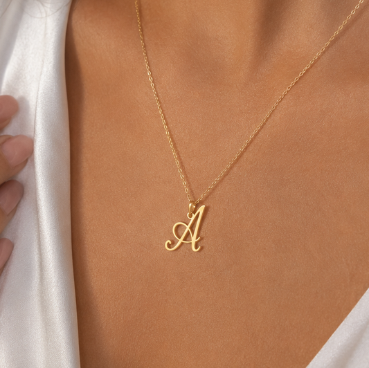 A delicate gold chain necklace with a cursive letter 'A' initial pendant, shown worn on a model's neck.