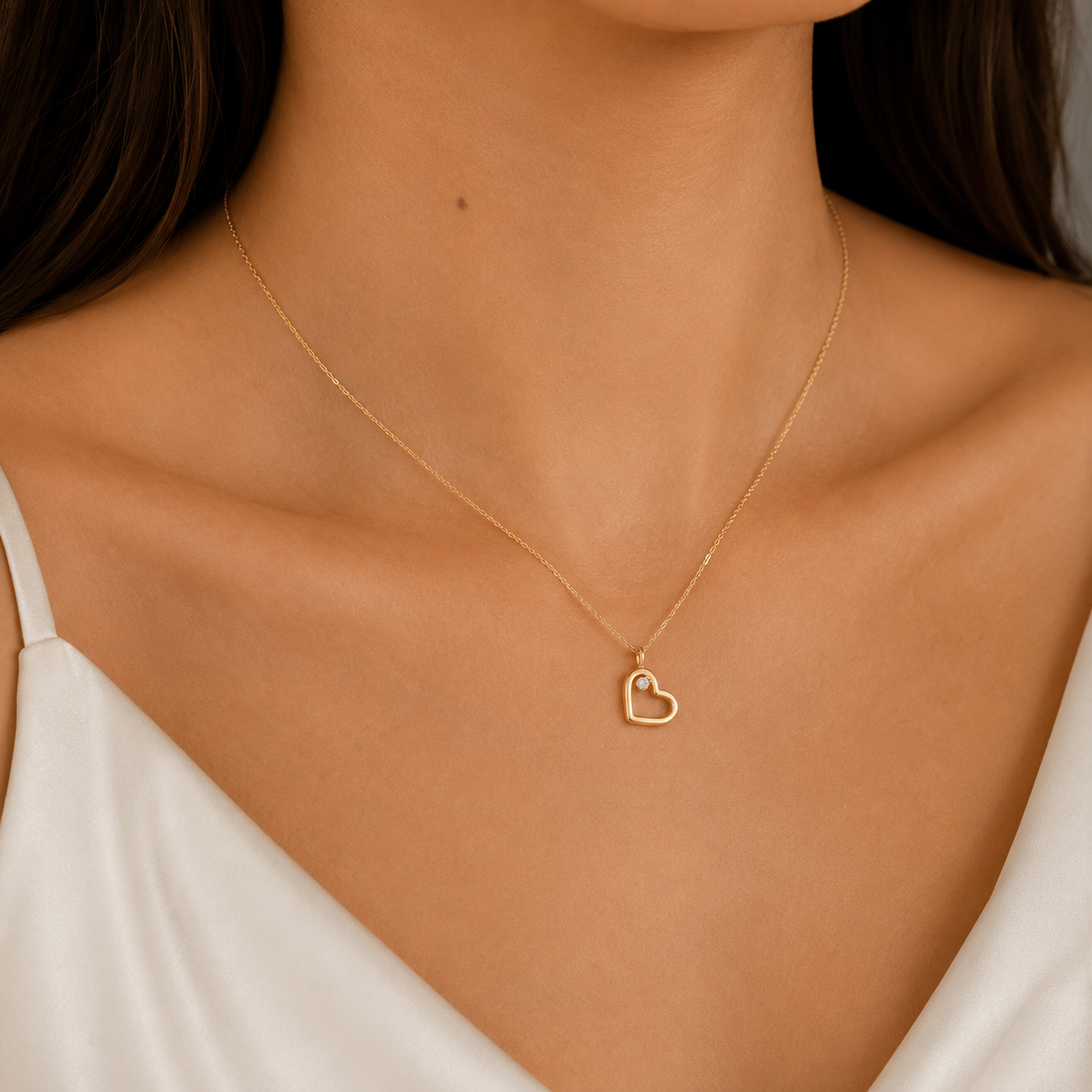 A delicate gold chain necklace with a small open heart pendant, worn by a model in a close-up shot.
