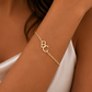 A delicate gold chain bracelet with interlocking initial letters 'BC' worn on a model's wrist, shown in a warm, close-up lifestyle shot.