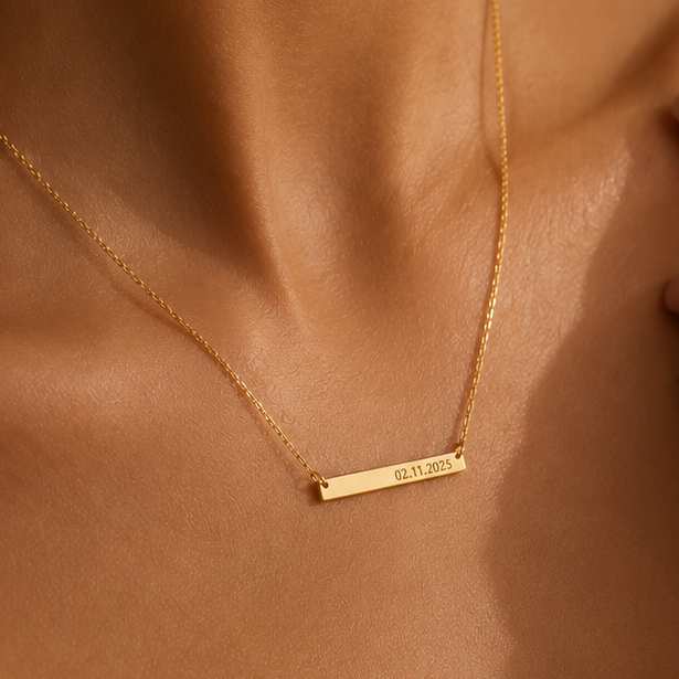 A delicate gold bar necklace with a personalized date engraved on it, worn on a model's neck.