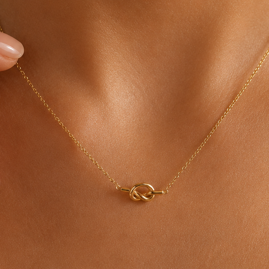 A delicate gold chain necklace with a small interlocking knot pendant, shown worn on a model's neck.