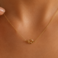 A delicate gold chain necklace with a small interlocking knot pendant, shown worn on a model's neck.