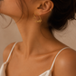 Woman wearing personalised Heart-Shaped Name Earrings in solid 18K yellow gold with a white satin dress.