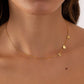 A delicate gold chain necklace worn by a model, featuring small letter charms 'M' and 'H' and a heart charm.