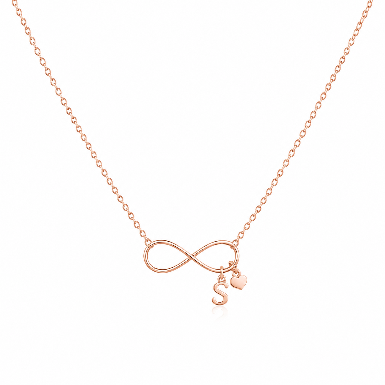 A delicate rose gold necklace featuring an infinity symbol pendant with a small hanging initial 'S' charm and a tiny heart, displayed on a clean white background.
