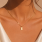 A delicate gold chain necklace with a small rectangular pendant engraved with the letter 'B', worn on a model's neck.