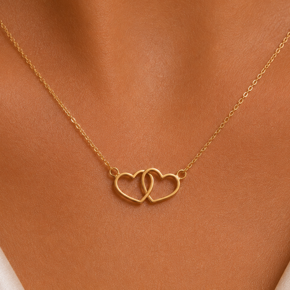 A delicate gold chain necklace with two interlocking open heart pendants, shown worn on a model's neck.