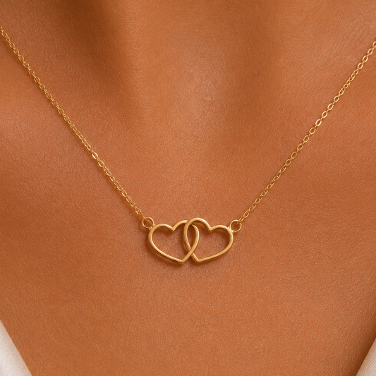 A delicate gold chain necklace with two interlocking open heart pendants, shown worn on a model's neck.