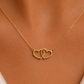 A delicate gold chain necklace with two interlocking open heart pendants, shown worn on a model's neck.