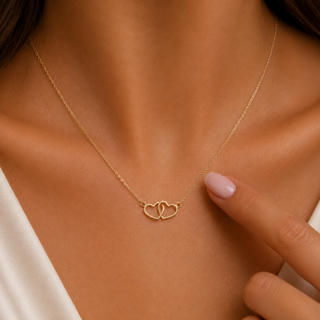 A delicate gold necklace with two interlocking open heart pendants, worn on a model's neck with a soft-focus background.