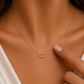 A delicate gold necklace with two interlocking open heart pendants, worn on a model's neck with a soft-focus background.