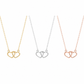 Three interlocking heart pendant necklaces on delicate chains, shown side by side in yellow gold, silver, and rose gold finishes against a plain white background.
