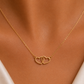 A delicate gold chain necklace with two interlocking open heart pendants, shown worn on a model's neck.
