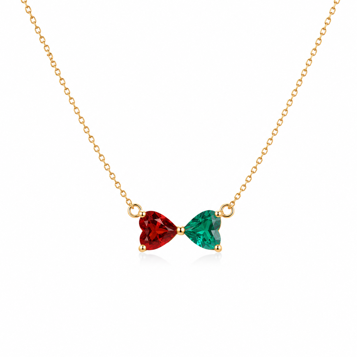 A gold chain necklace featuring a bow-shaped pendant with one red ruby heart gemstone and one green emerald heart gemstone in gold settings, shown on a plain white background.