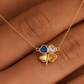 A gold necklace with a four-leaf clover pendant featuring heart-shaped blue, clear, and yellow inlays, shown worn on a hand.