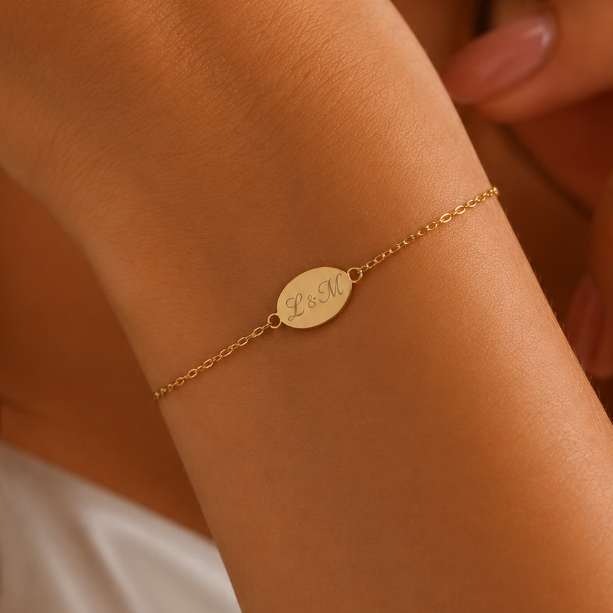 A delicate gold chain bracelet with a small oval engraved disc charm, worn on a woman's wrist.