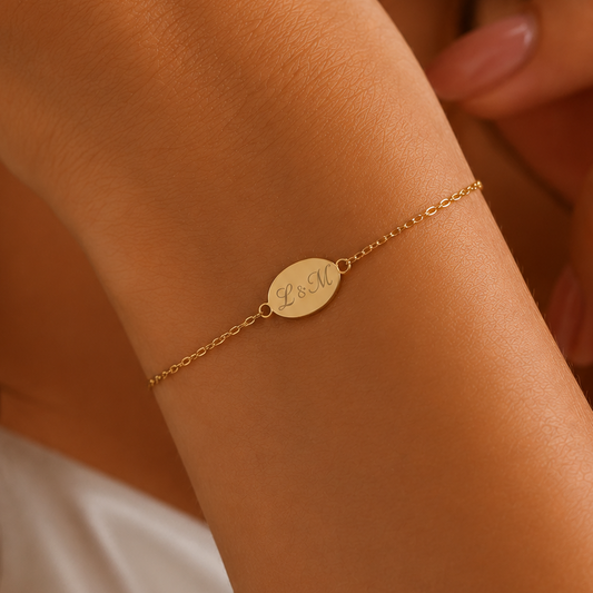 A delicate gold chain bracelet with a small oval engraved disc charm, worn on a woman's wrist.