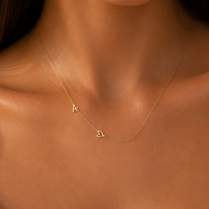 A close-up of a model wearing a delicate gold necklace with two small letter pendants, one reading 'A' and the other a triangle, styled with a white satin camisole.