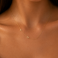 A close-up of a model wearing a delicate gold necklace with two small letter pendants, one reading 'A' and the other a triangle, styled with a white satin camisole.