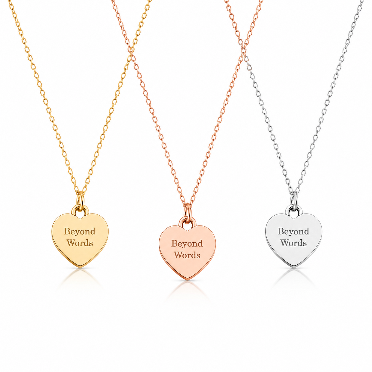 Three heart-shaped pendant necklaces on delicate chains, shown in yellow gold, rose gold, and silver finishes. Each heart pendant is engraved with the words 'Beyond Words' on a clean white background.