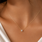 A delicate gold chain necklace with a single round-cut clear gemstone pendant, shown worn on a model's neck.