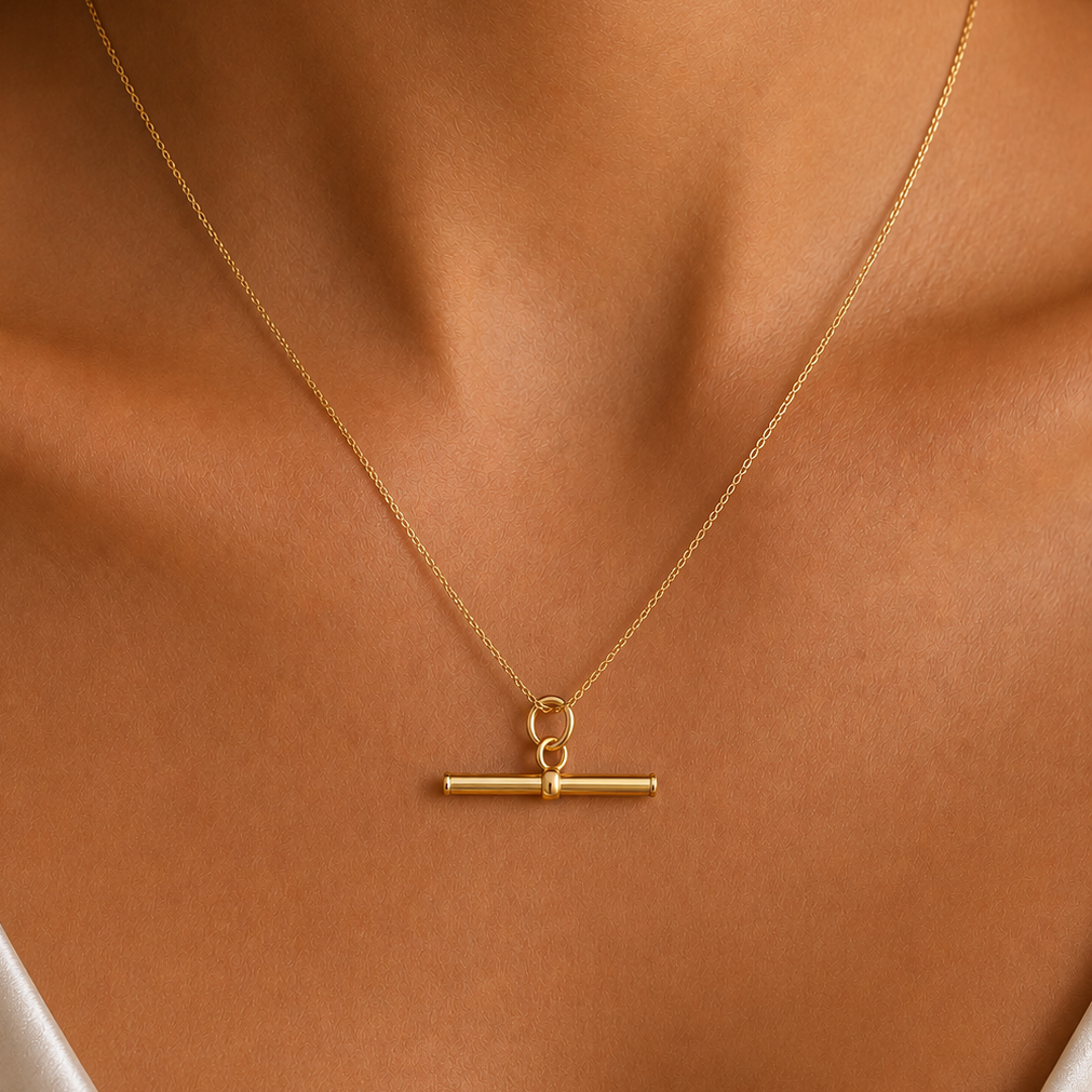 A delicate t-bar gold necklace with a horizontal bar pendant and a small top ring, shown worn on a model's neck.
