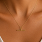A delicate t-bar gold necklace with a horizontal bar pendant and a small top ring, shown worn on a model's neck.