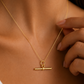 A close-up of a model wearing a delicate t bar gold necklace with a horizontal bar toggle pendant, styled with a white satin top.