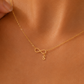 A close-up of a model wearing a delicate gold necklace with an infinity symbol and a small letter 'S' pendant, styled with a white satin camisole.