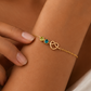 A delicate gold chain bracelet with a double heart design and small colorful gemstone accents, shown worn on a woman's wrist.