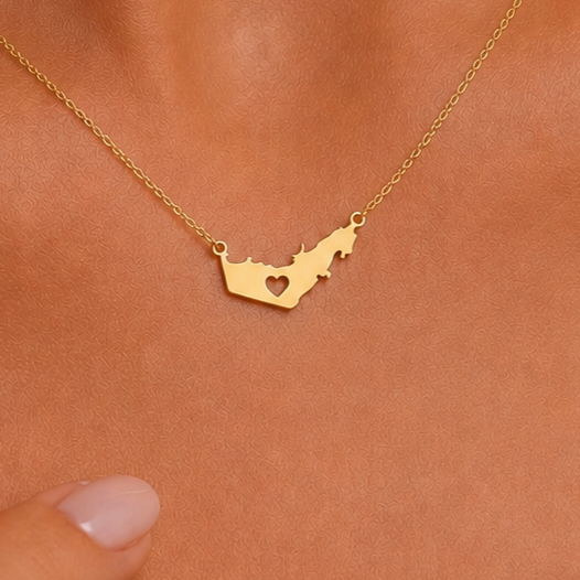 A gold necklace with a UAE map-shaped pendant featuring a heart cutout, shown worn on a person's neck.