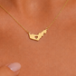 A gold necklace with a UAE map-shaped pendant featuring a heart cutout, shown worn on a person's neck.