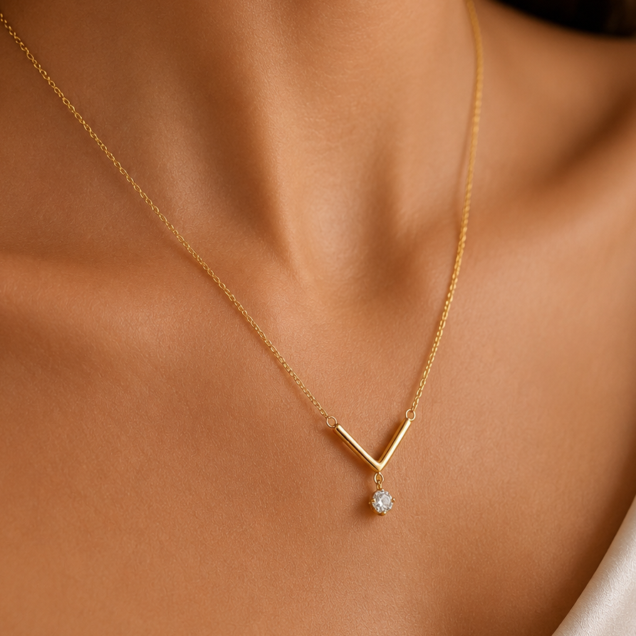 A delicate gold V-shaped necklace with a small clear teardrop gemstone pendant, shown worn on a model's neck.