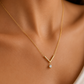A delicate gold V-shaped necklace with a small clear teardrop gemstone pendant, shown worn on a model's neck.
