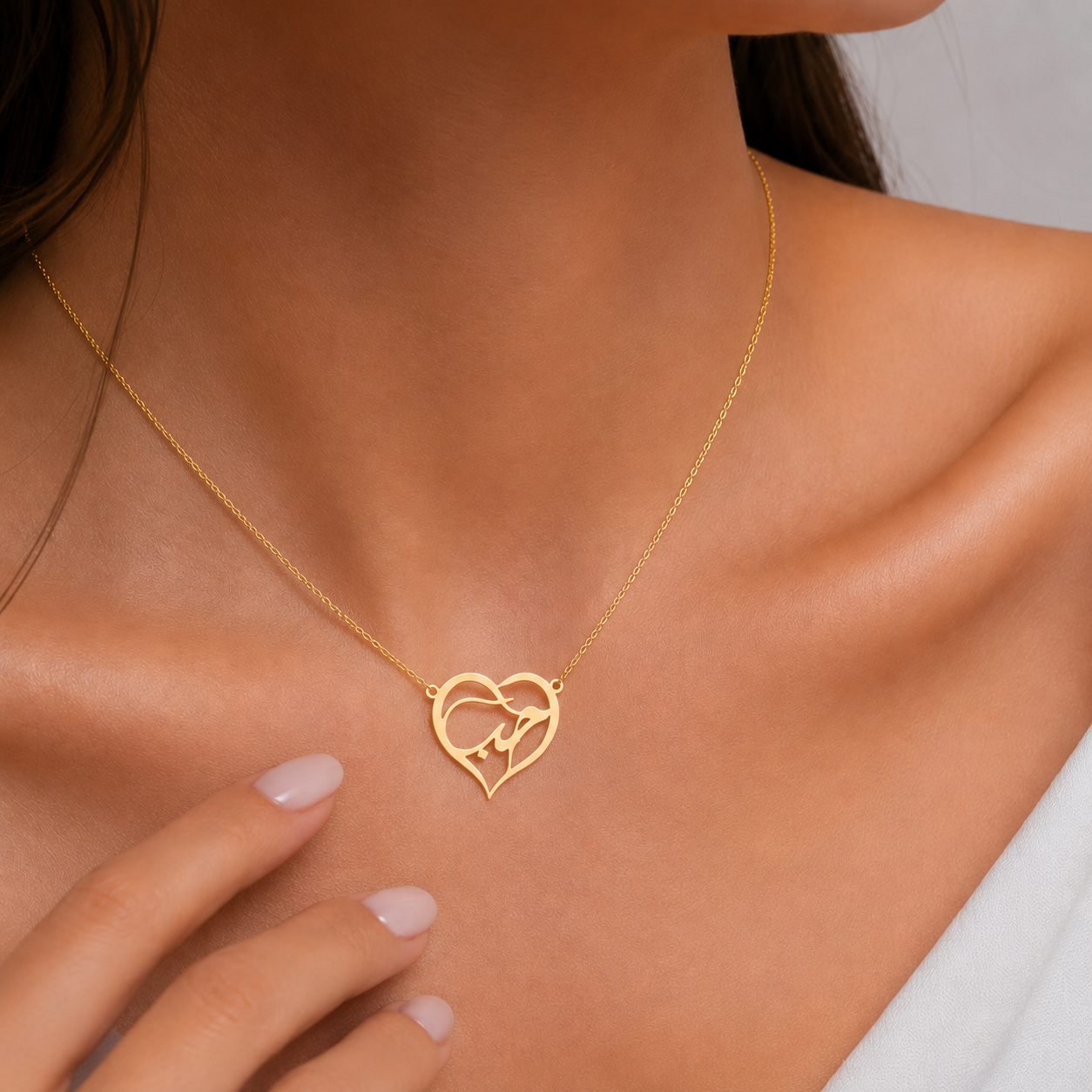 A close-up of a woman's neck and chest wearing a delicate gold necklace with an open heart pendant featuring a small bird design, styled with a white top.