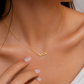 A delicate gold chain necklace with a small Arabic calligraphy pendant, shown worn on a model's neck with her hand resting near the chest.