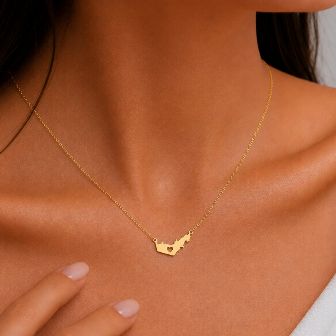 A close-up of a model's neck and chest wearing a delicate gold chain necklace with a small gold UAE shaped pendant